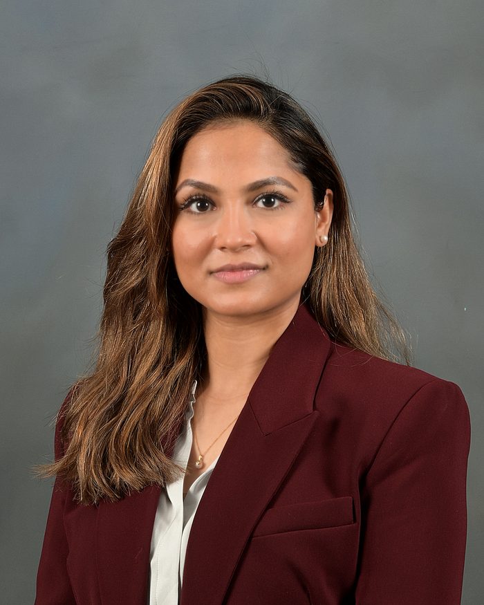 Quick LinkedIn headshot taken elsewhere — flat lighting and washed-out gray backdrop, woman in burgundy blazer