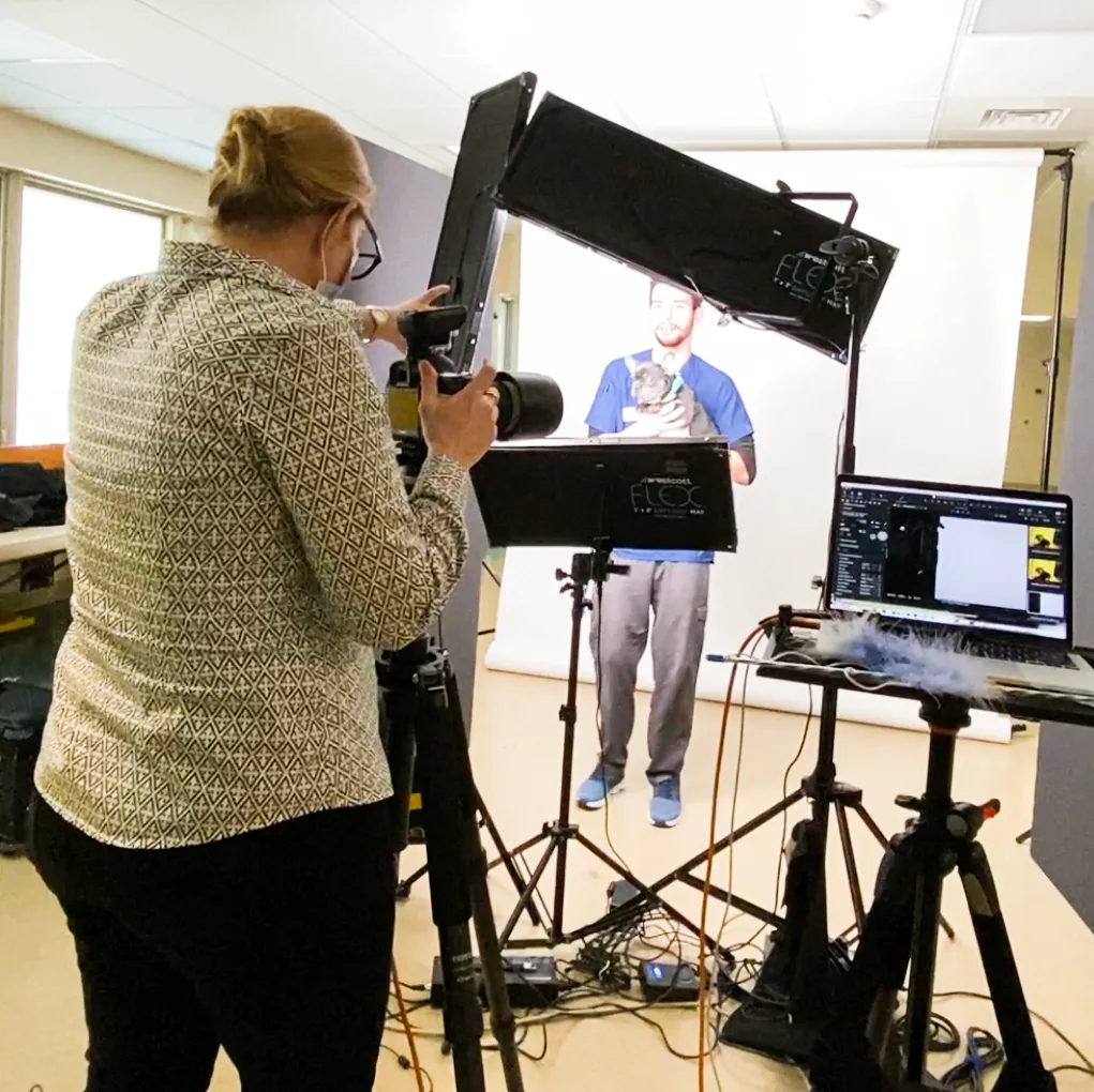 Behind the scenes — Isolde Baylor VMD photographing a veterinary team member with a small dog patient on a portable studio backdrop set up inside an animal hospital