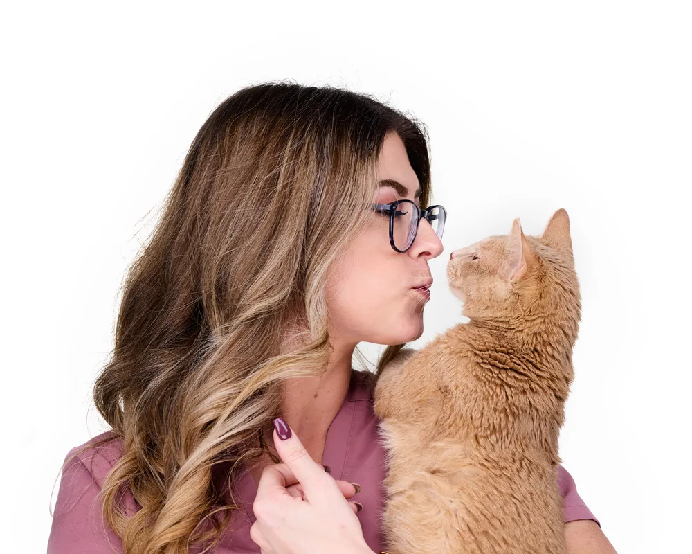 Veterinary professional in pink scrubs sharing a moment with an orange tabby clinic cat — on-site team headshot photography by Isolde Baylor VMD